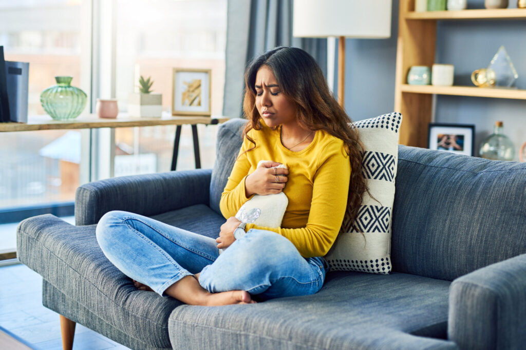 Young women holding a heart covered hot water bottle after an online abortion, she didn't know it would be so hard.